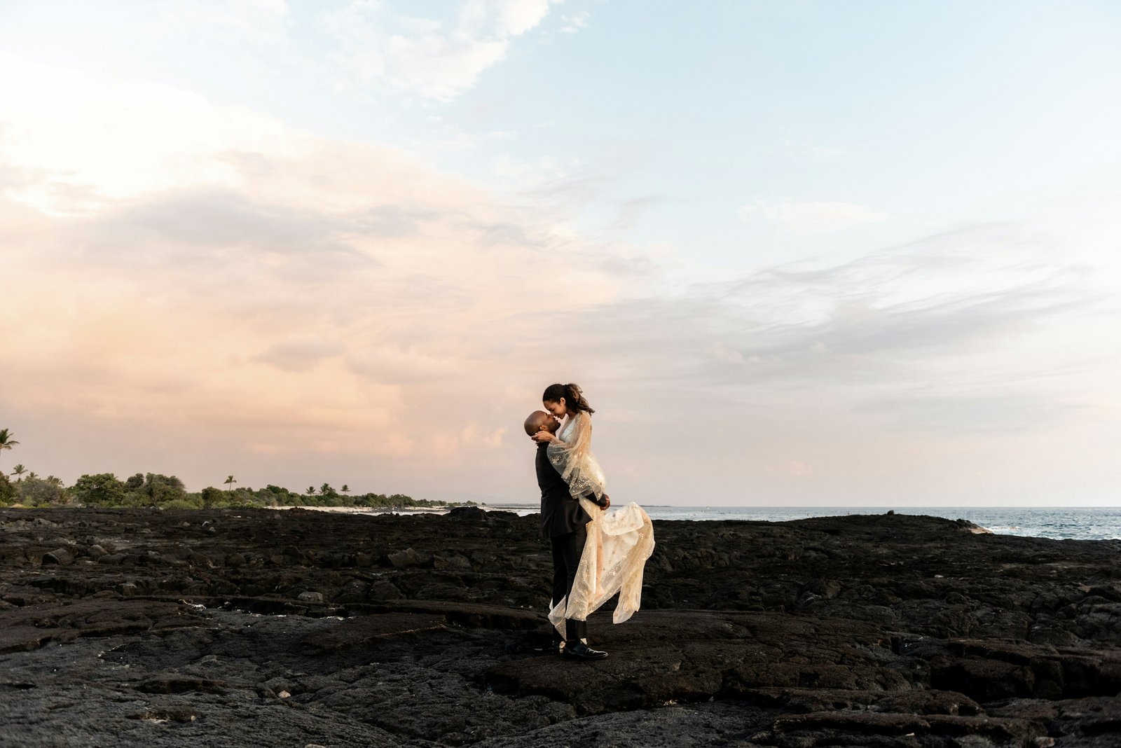 A couple embracing at sunset on a rocky coastline during a vow renewal
