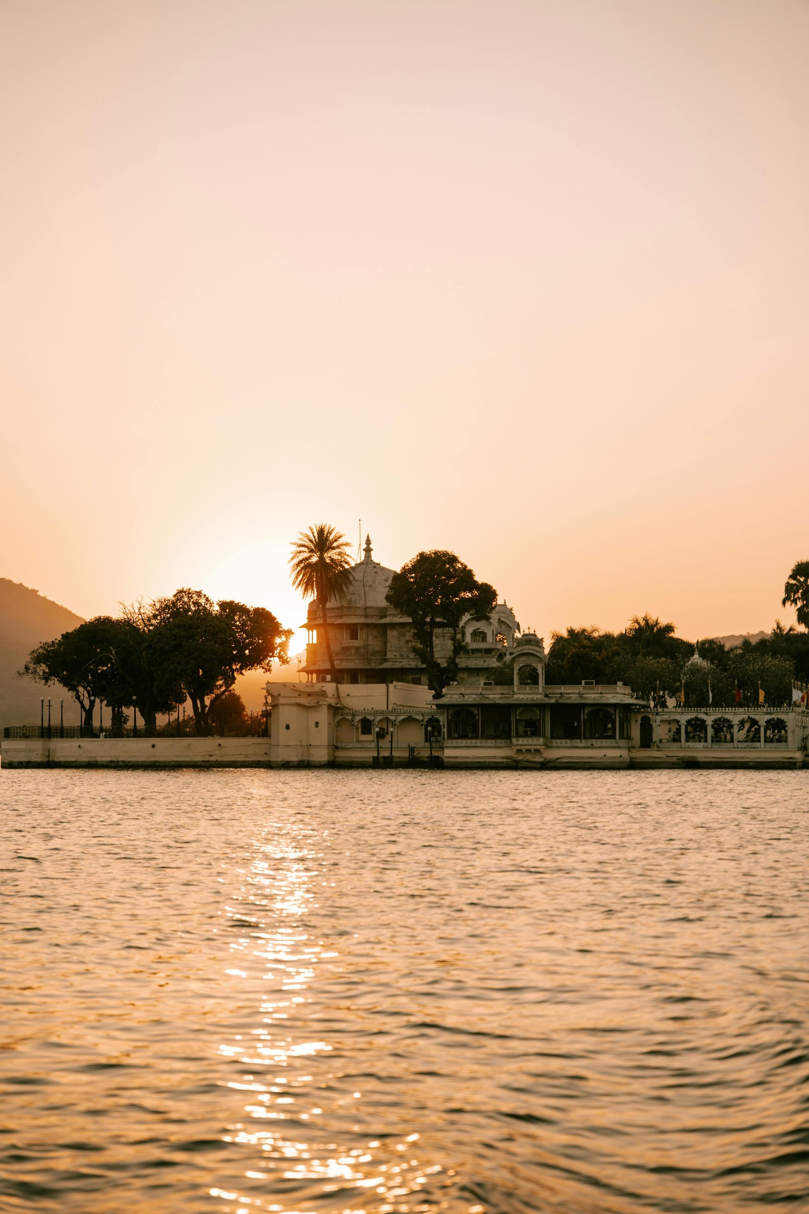 A heritage palace silhouetted against a golden sunset over Lake Pichola, Udaipur